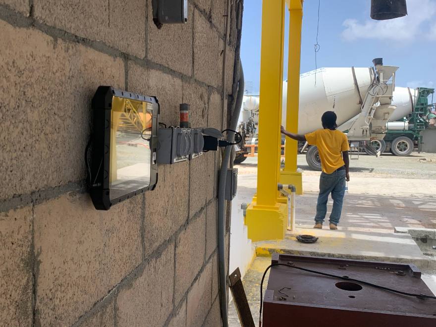 PunchClock clock mounted on a concrete block wall at a construction yard, mixer trucks behind