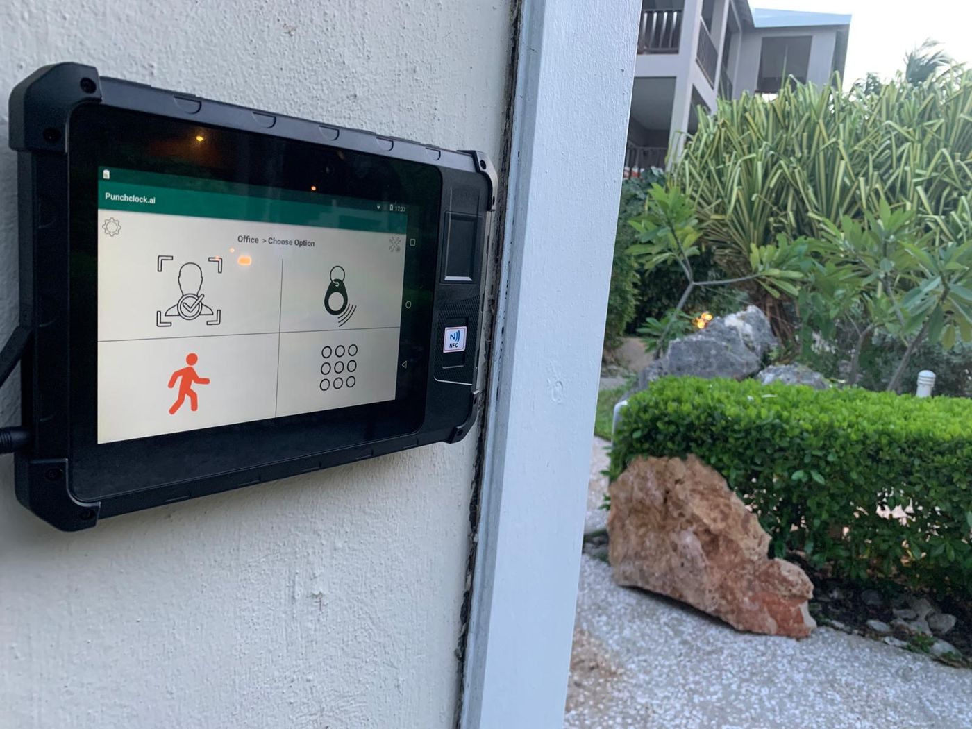 PunchClock clock mounted on an outdoor wall, screen showing the face, keyfob and pinpad clock-in options